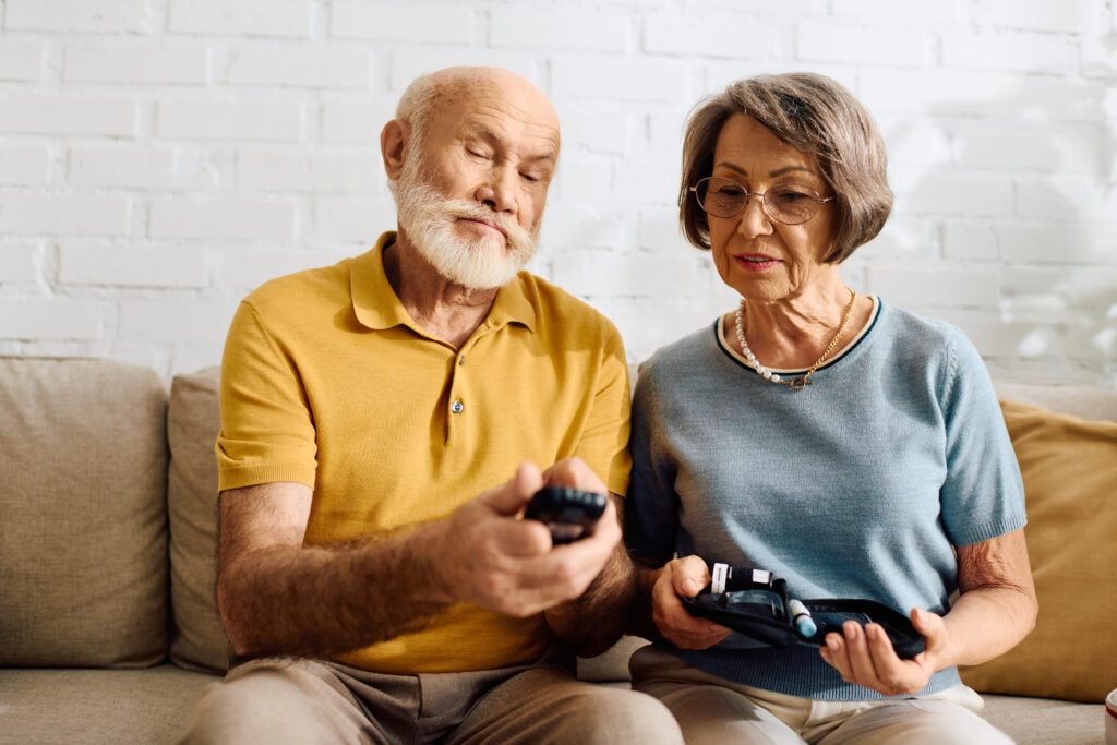 An elderly couple sits together reviewing their glucose meters and diabetes supplies at home.