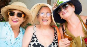 Three senior women friends smiling together in summer hats